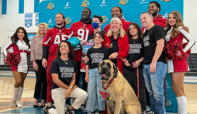 AZ Cardinal players, cheerleader and dog posing for group photo with Kevin and his family and a staff member